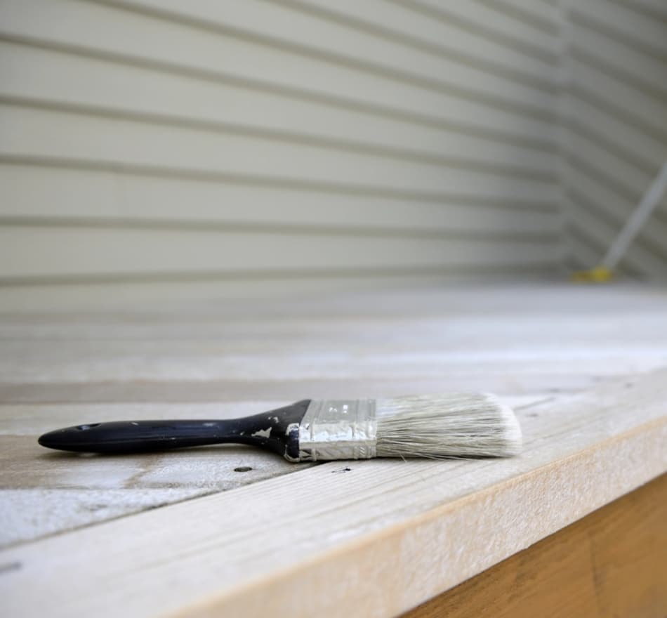 Close-up of a paintbrush resting on a wooden surface with freshly painted slats in the background.